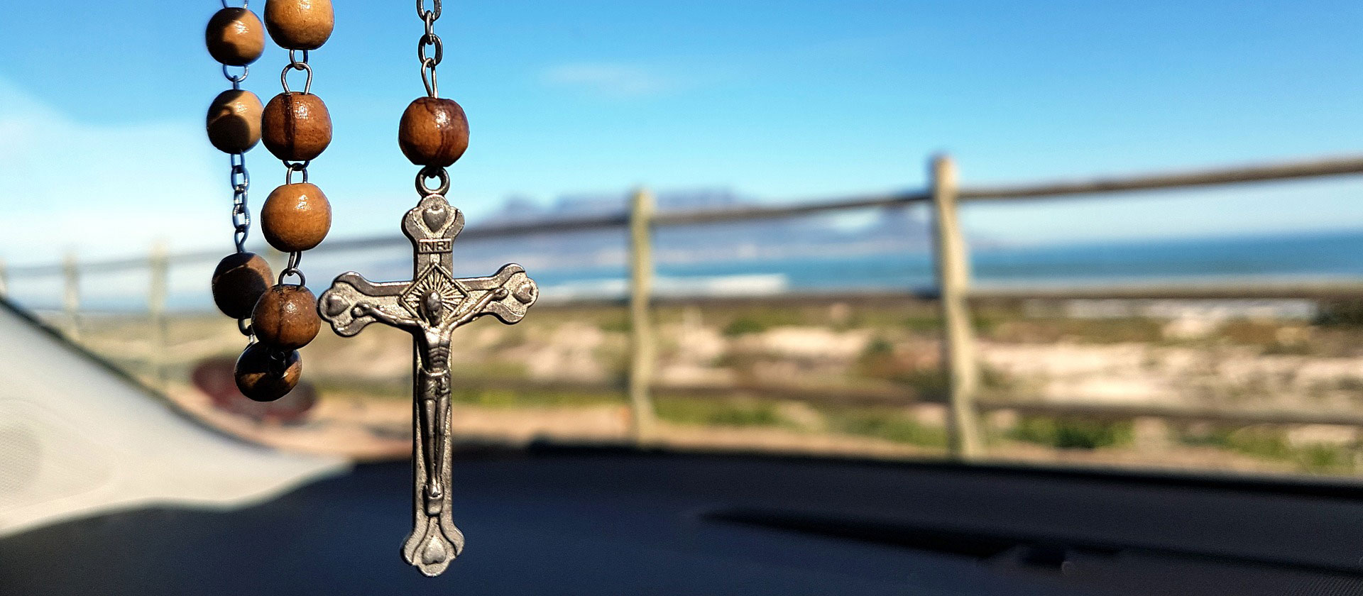 Rosary hanging in car with ocean view in background